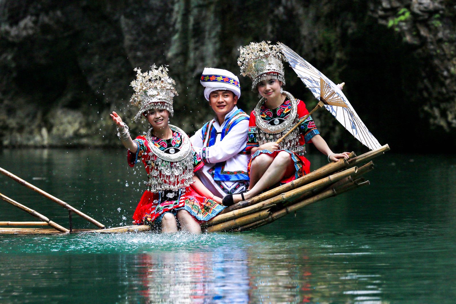 Three people in traditional dress riding a bamboo raft on the Ayi River